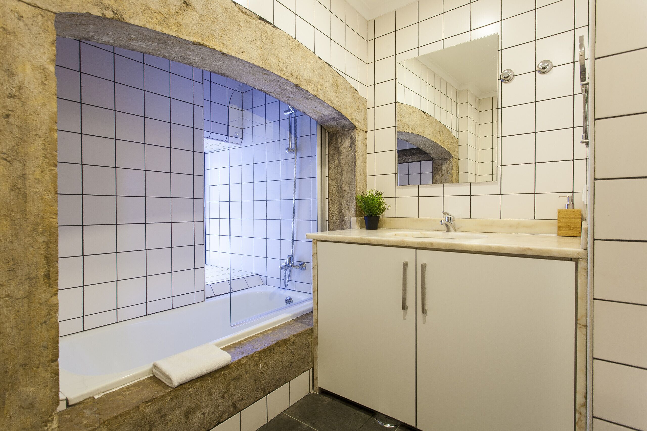 Un baño con bañera, lavamanos, espejo y una planta en maceta.