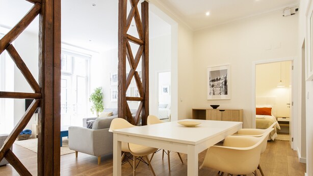 Un interior moderno con una mesa de comedor blanca, sillas color beige y una pared de acento de madera.