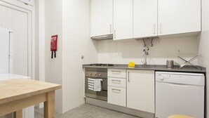Cocina compacta con armarios blancos, estufa, horno y lavavajillas.