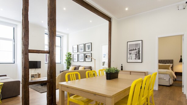 A modern living space with a wooden dining table, yellow chairs, a sofa, and a television.