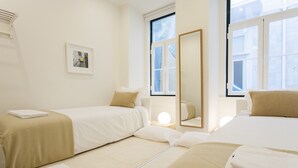A hotel room with two beds, a bedside table, a mirror, and a window.