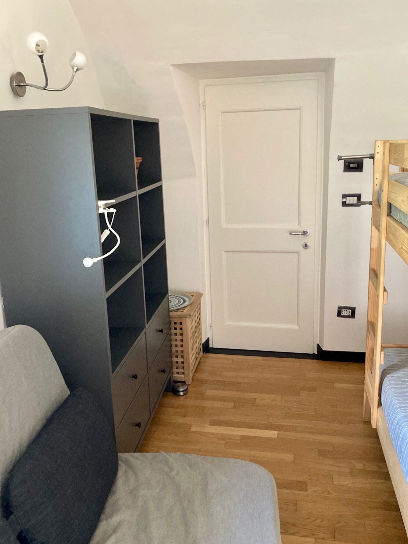 Ein Schlafzimmer mit einem grauen Kleiderschrank, einem hölzernen Bett, einer weißen Tür und einem kleinen Wäschekorb.