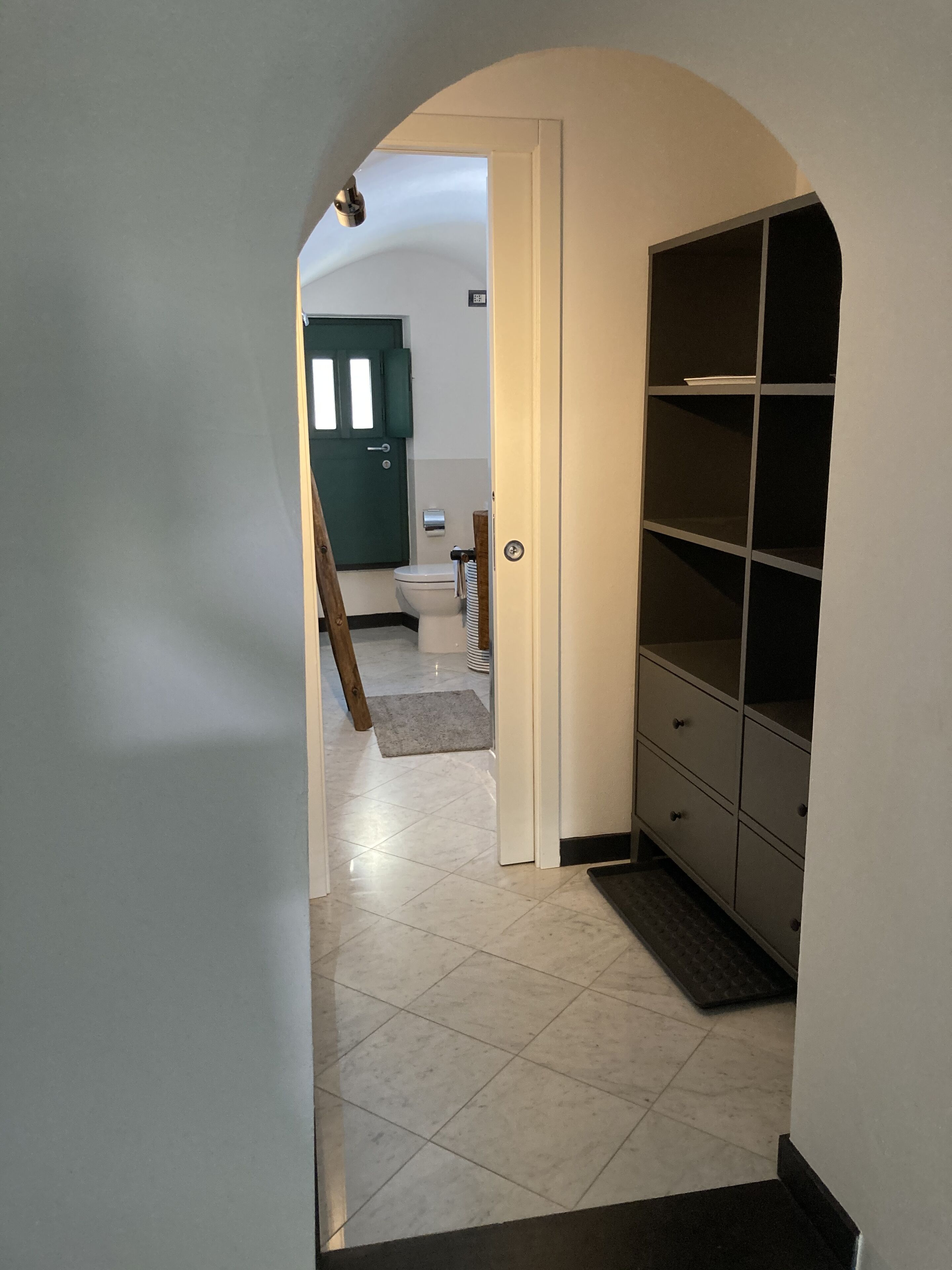 En hall med ett klinkergolv, en grön dörr, en vit toalett och ett förvaringsskåp med flera lådor.