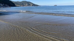A beach with clear water, a sandy shore, and a mountainous backdrop.
