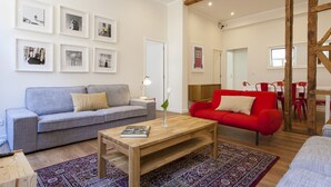 A modern living room with a grey sofa, a red sofa, a wooden coffee table, and a patterned rug. There are framed pictures on the wall and a wooden beam structure in the background. - Central Downtown 3D up to 17guests by Central Hill (Lisboa ciudad)