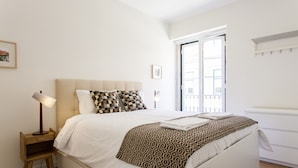 Una cama bien hecha con una manta estampada, una lámpara de noche y una mesita de noche de madera.