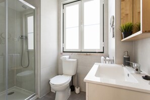 A modern bathroom with a glass-enclosed shower, a toilet, a sink, and a window above the toilet.