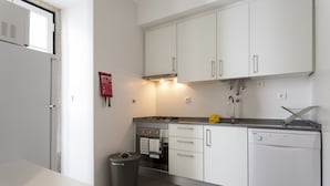 Cocina compacta con alacenas blancas, estufa a gas, horno, lavavajillas y un cubo de basura.
