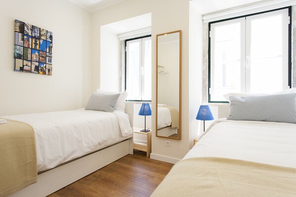 A room with two beds, a large mirror, and a window with a view of the outside.