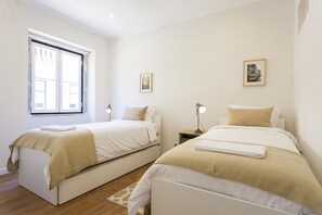 A bedroom with two beds, a window, and two bedside tables with lamps.