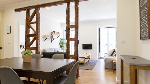 Una sala de estar moderna con una mesa de comedor de madera, sillas grises, un sofá y una televisión.