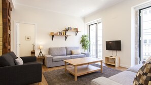 Una sala de estar moderna con un sofá gris, un sillón negro, una mesa de centro de madera y una estantería.