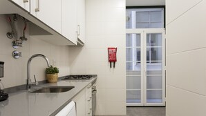 A modern kitchen with a stainless steel sink, a gas stove, and a built-in dishwasher. There is a window with frosted glass doors and a fire safety sign on the wall.