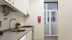 Cocina moderna con un lavamanos de acero inoxidable, estufa a gas y lavavajillas integrado. Hay una ventana con puertas de vidrio esmerilado y un letrero de seguridad contra incendios en la pared.