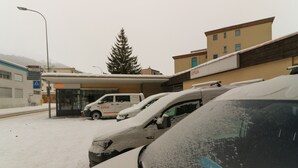 Ein Gebäude mit überdachter Einfahrt, einem parkenden Lieferwagen und mehreren Autos, die mit Schnee bedeckt sind.