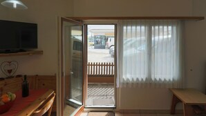 Ein Zimmer mit einer Schiebetür zum Balkon, einem Holztisch, einer Bank und einem Fernseher auf einem Regal.
