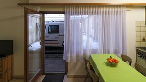 Ein Zimmer mit Esstisch, Stühlen, einem Fernseher auf einer Holzkommode, einer Küchenzeile mit Herd und einer Schiebetür zu einem Parkplatz mit einem weißen Lieferwagen.