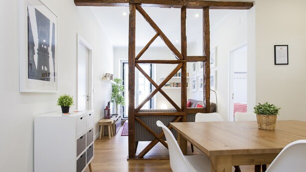 Ein Essbereich mit Holztisch und weißen Stühlen, einem weißen Schrank mit Schubladen sowie einer Holzwand mit Kreuzgittermuster.