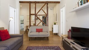 Ein Wohnzimmer mit einer Couch, einem roten Kissen, einem Holz-TV-Schrank und einem Fernseher.