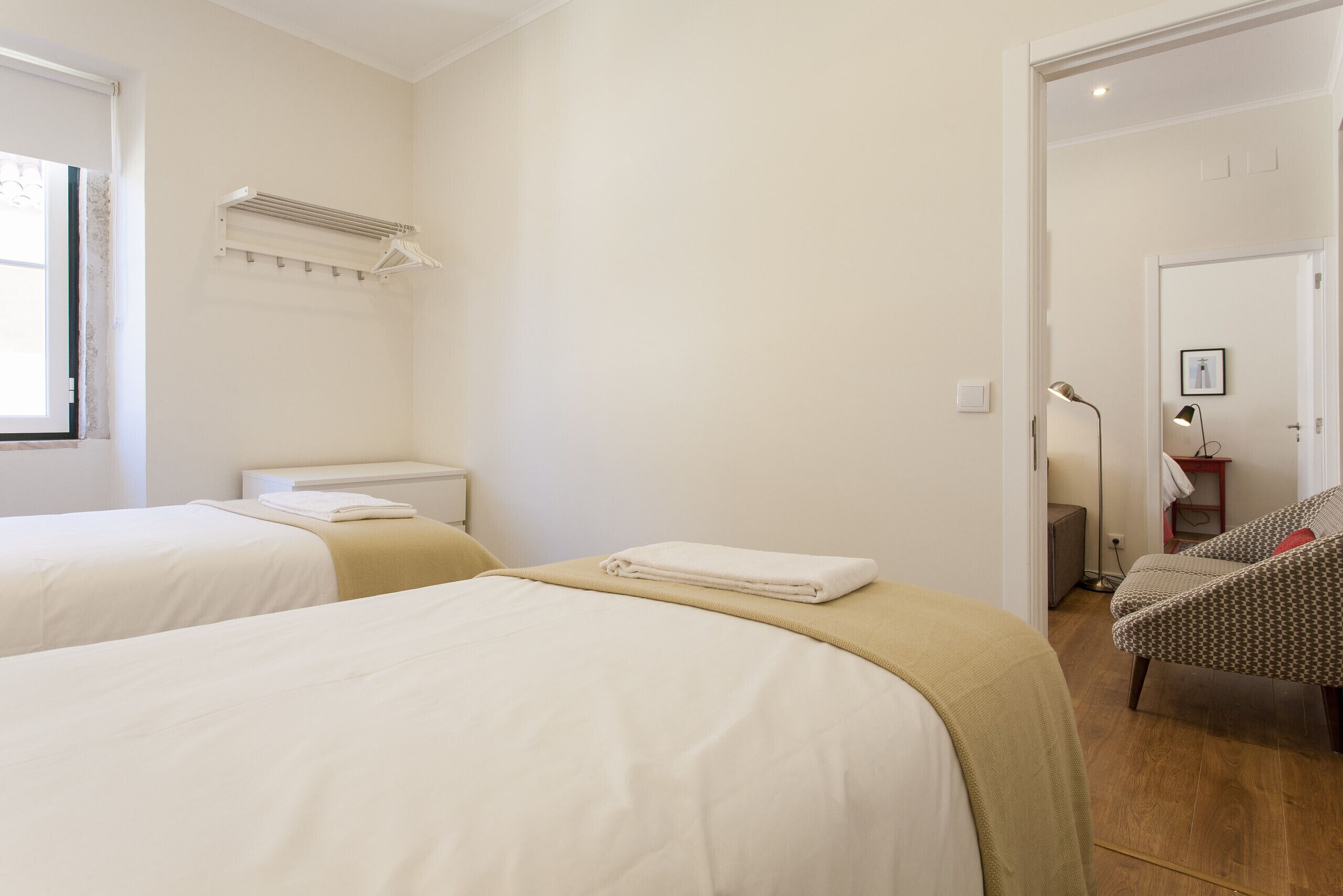 A hotel room with two beds, a heater, a chair, and a door leading to another room.