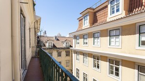 Ein schmaler Balkon mit grüner Reling, der auf eine Häuserzeile mit zahlreichen Fenstern und einem Ziegeldach blickt.
