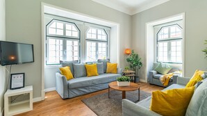 A spacious living room with a grey sofa, yellow cushions, a coffee table, and large windows. - Central Chiado RC by Central Hill (Lisboa ciudad)