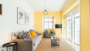 A living room with a sofa, armchair, and a coffee table. There is a TV on a stand and a lamp on a side table.
