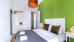 A modern bedroom with a large bed, a green accent wall, a hanging light fixture, and a white nightstand.
