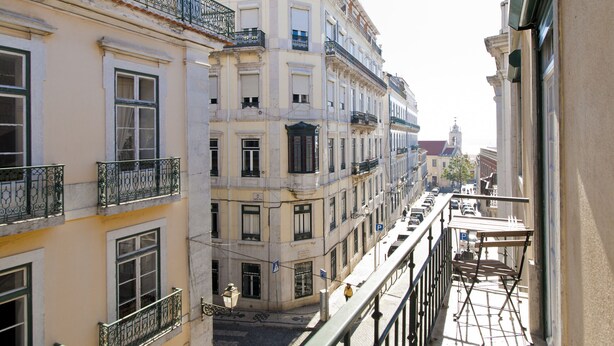 A narrow street with multi-story buildings, balconies, and a clear view of the street below.