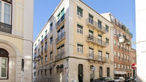 A multi-story building with balconies, a street in front, and parked cars.
