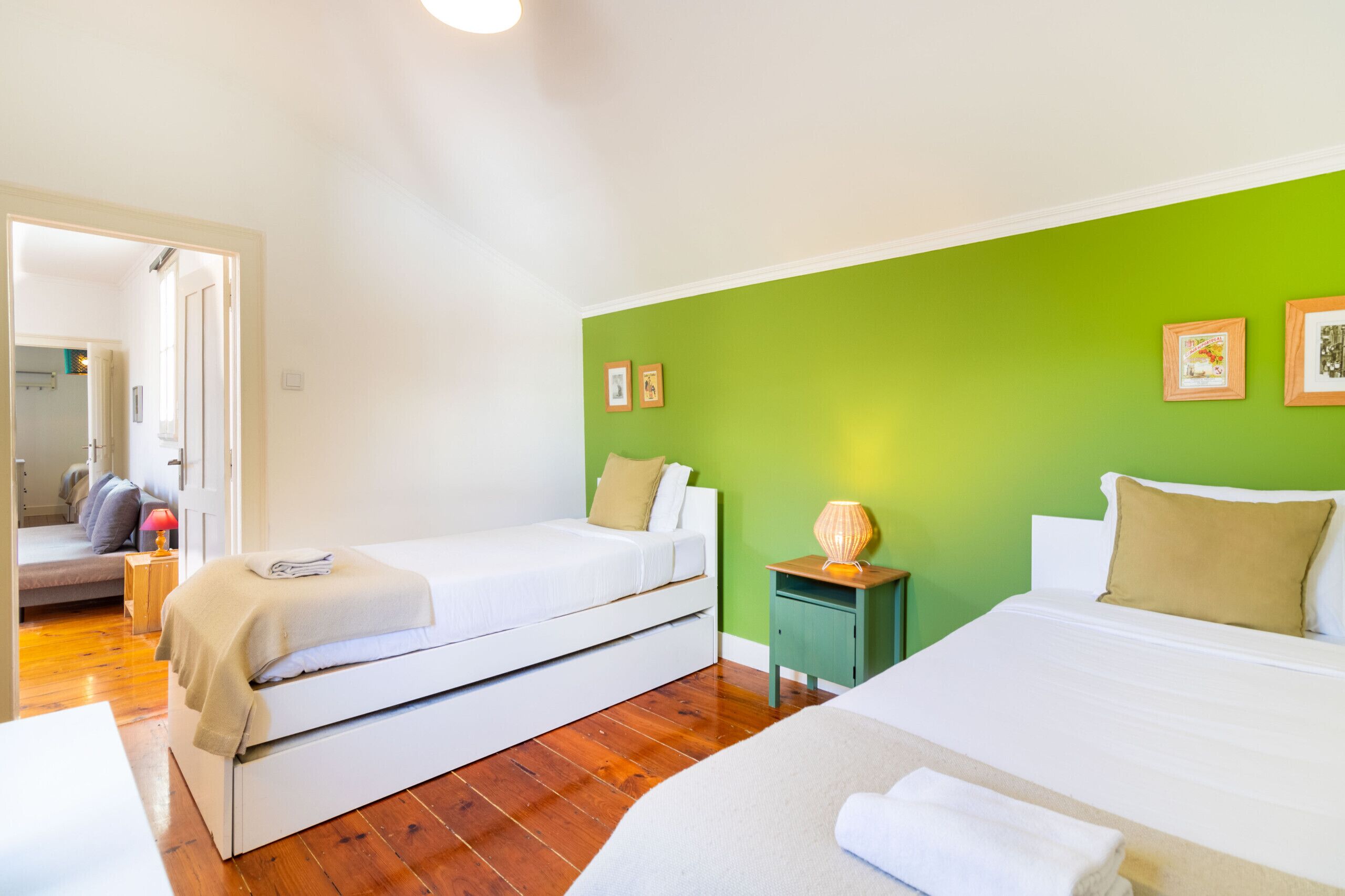 A hotel room with two beds, a green accent wall, and a wooden floor.