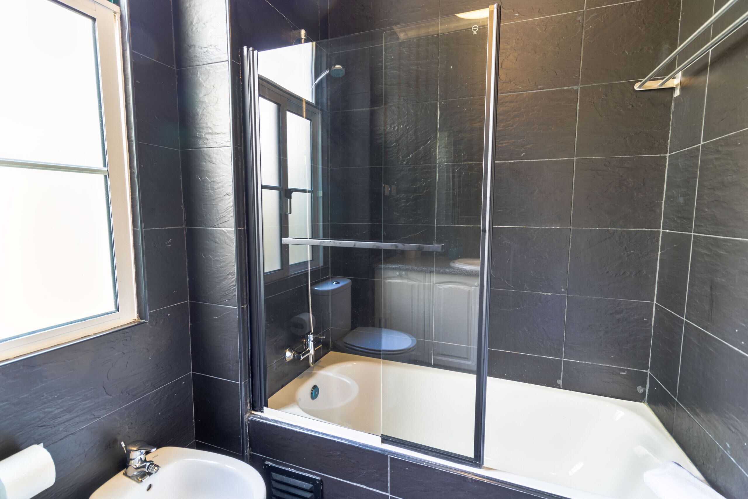 A modern bathroom with a glass-enclosed shower, a white bathtub, and a toilet.