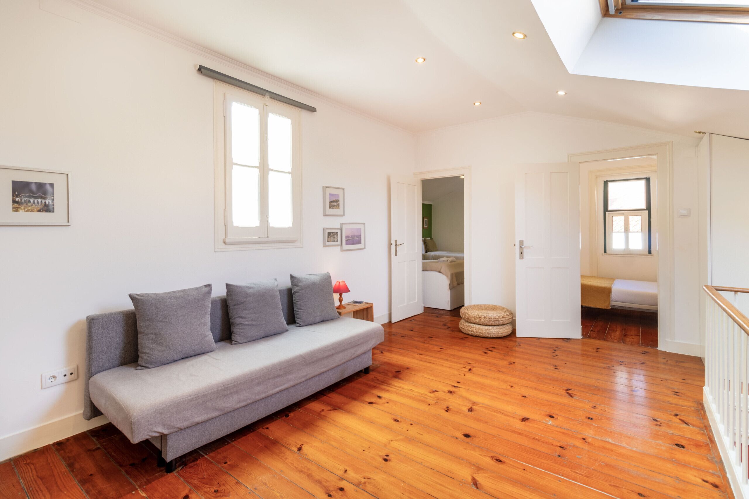 Een ruime kamer met houten vloer, een grijze bank en dakraam.