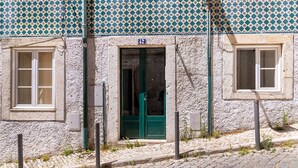 Un edificio con calle adoquinada, puerta verde y tejado de patrón azul y amarillo.