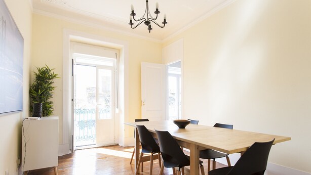 Un comedor con una mesa de madera y sillas negras, un armario blanco y una planta en maceta.