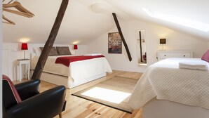 Un dormitorio con techo inclinado, una cama, una silla, una mesita de noche y una lámpara.