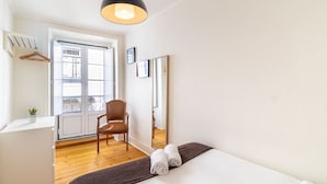A hotel room with a bed, a desk, a chair, a large mirror, and a window with a view of buildings.