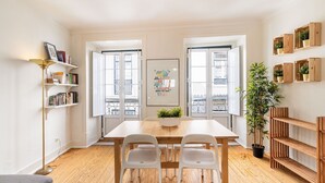 A dining area with a wooden table and chairs, a bookshelf, a potted plant, and a framed artwork on the wall.