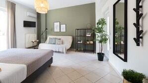 Un dormitorio moderno con una cama grande, una mesita de noche, un televisor, una estantería y una planta en maceta.