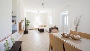 Una sala moderna con sofá, mesa de centro y mesa de comedor. Hay una planta y un jarrón sobre la mesa.
