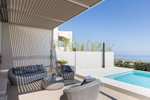 Ein moderner Außenbereich mit Pool, Sitzgelegenheiten und Meerblick.