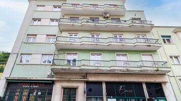 Um edifício com vários andares e varandas, restaurante chamado 'Enora' no térreo e um caixa eletrônico visível.