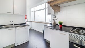 A modern kitchen with white cabinetry, a dishwasher, a stove, and a window providing natural light.