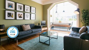 A living room with a sofa, a coffee table, and a TV. There are framed pictures on the wall and a large window with a view.