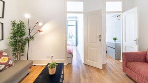 Ein modernes Wohnzimmer mit einer Couch, einem Couchtisch mit Pflanze, einer Stehlampe und einem Flur, der in einen anderen Raum führt.