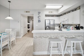 A modern kitchen with white cabinetry, a central island with stools, and a dining area with white chairs.