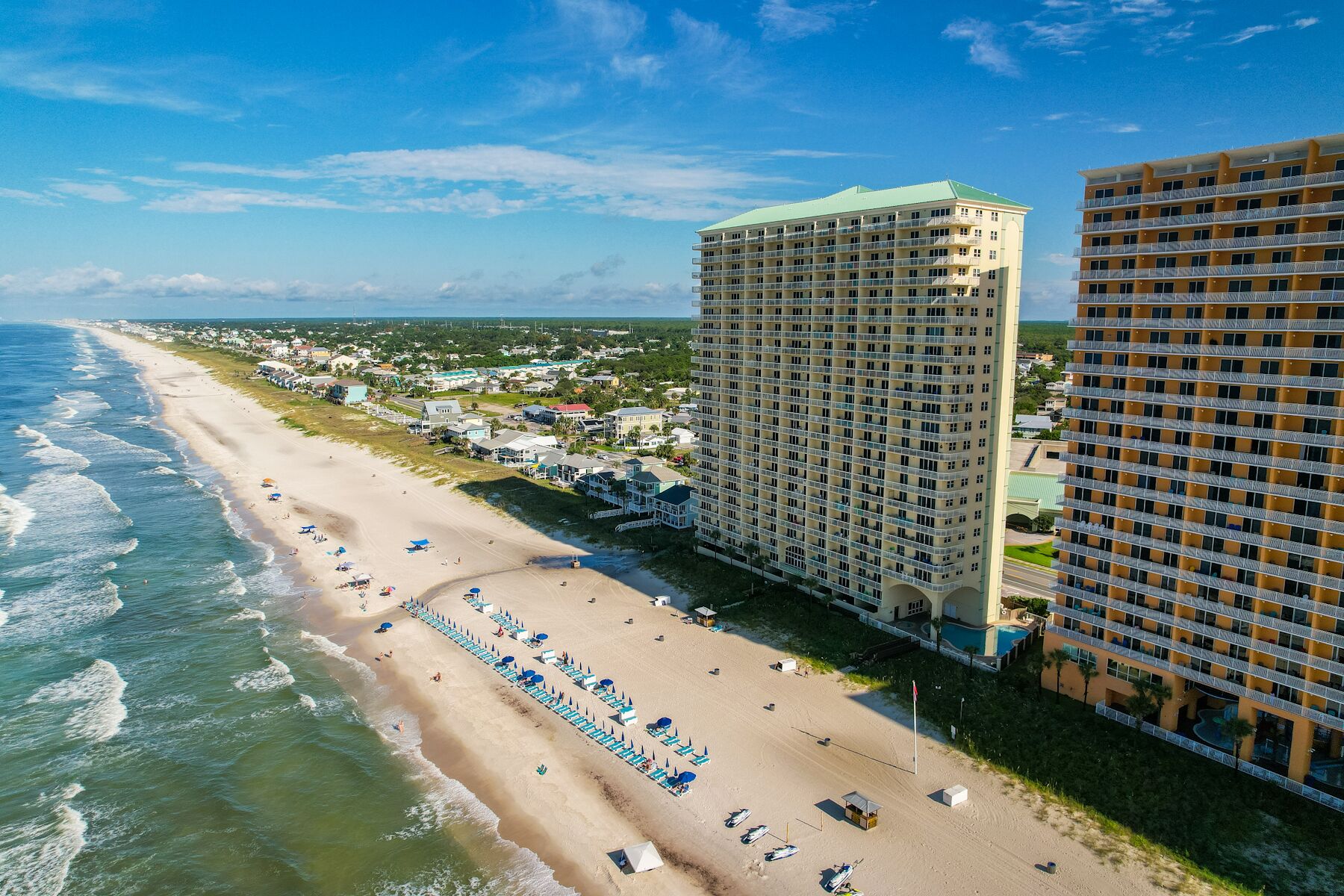 Ein Strandhotel mit mehreren Etagen, ein Sandstrand mit Sonnenschirmen und Blick auf den Ozean.