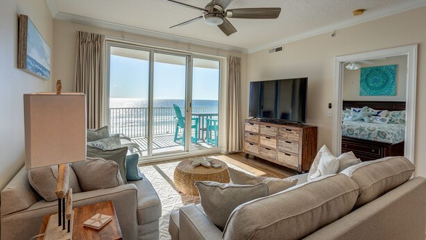 A hotel room with a balcony, a TV, a sofa, and a wooden dresser. - 2 Bedroom in Ocean Villa Resort -  Beautifully decorated and appointed condo with amazing views! (Panama City Beach)