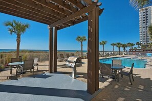Relax by the pool surrounded by lounge chairs and a barbecue grill, under a shaded pergola.