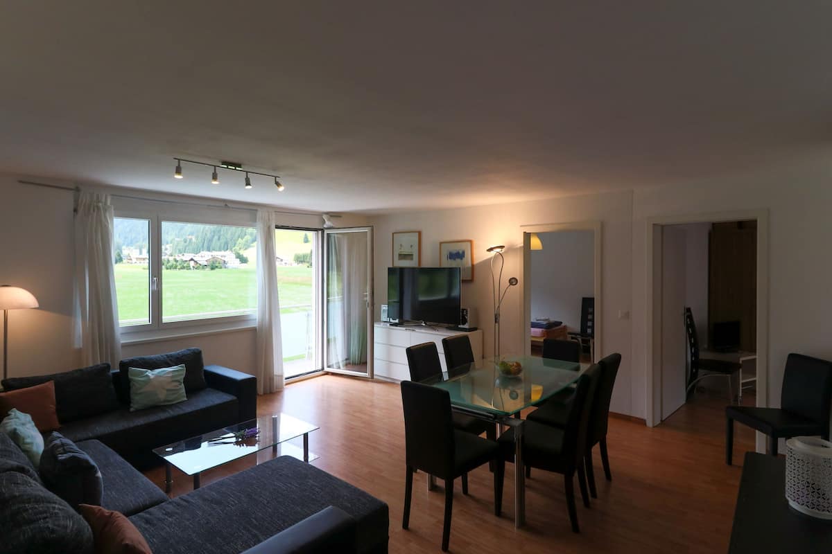 A modern living room with a glass dining table, sofas, and a TV.